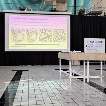 Auf der Leinwand sieht man den aktuellen Stand der Planung, davor ein Podest, wo Carmen Baumann den Ablauf erklärt.