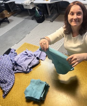 Ich sitze am Tisch, lächle in die Kamera und halte einen grünen Lappen in der Hand.