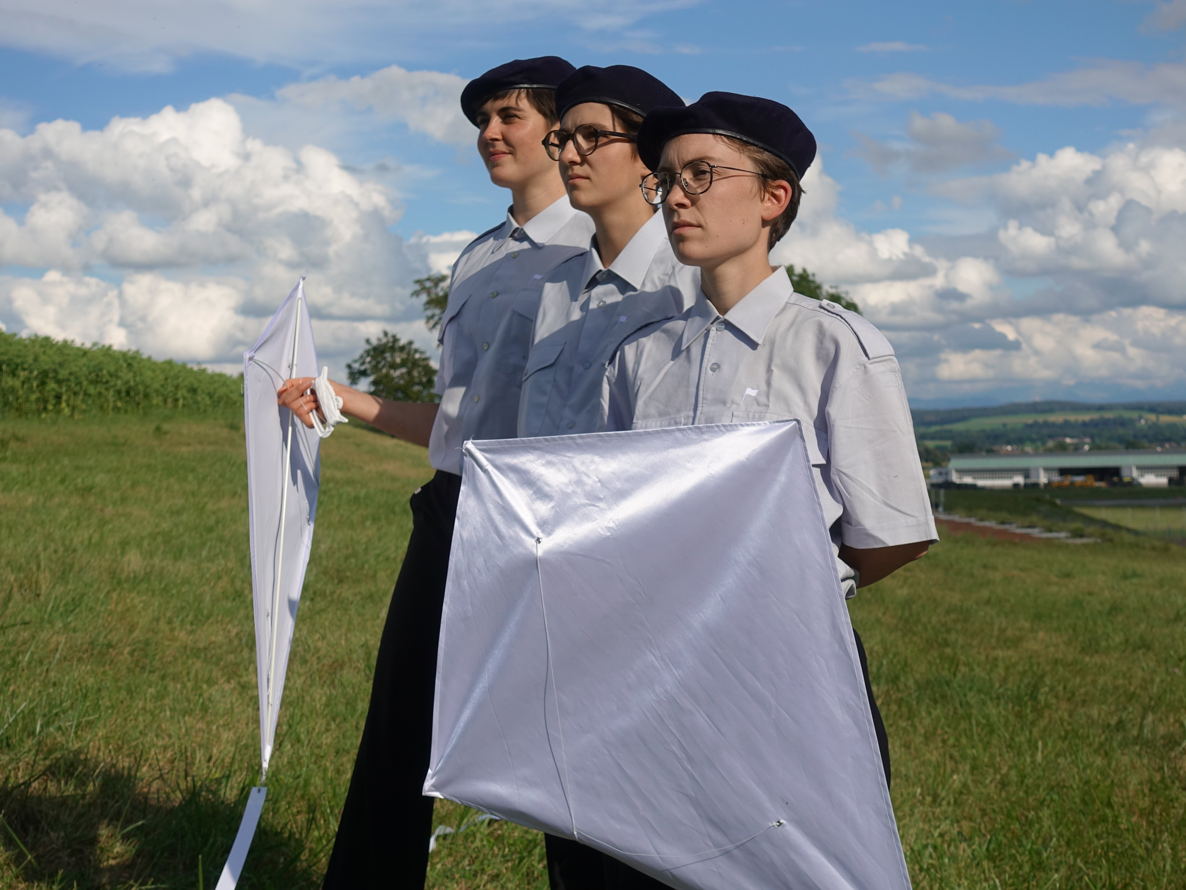Drei Frauen in militärischer Uniform auf einer Wiese mit weissen Drachen in der Hand.
