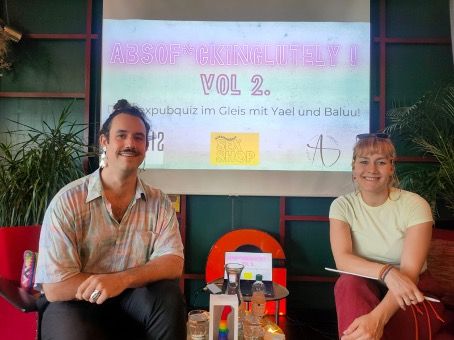 Baluu und Yael die Hosts der Sexpubquizes vor einer Leinwand