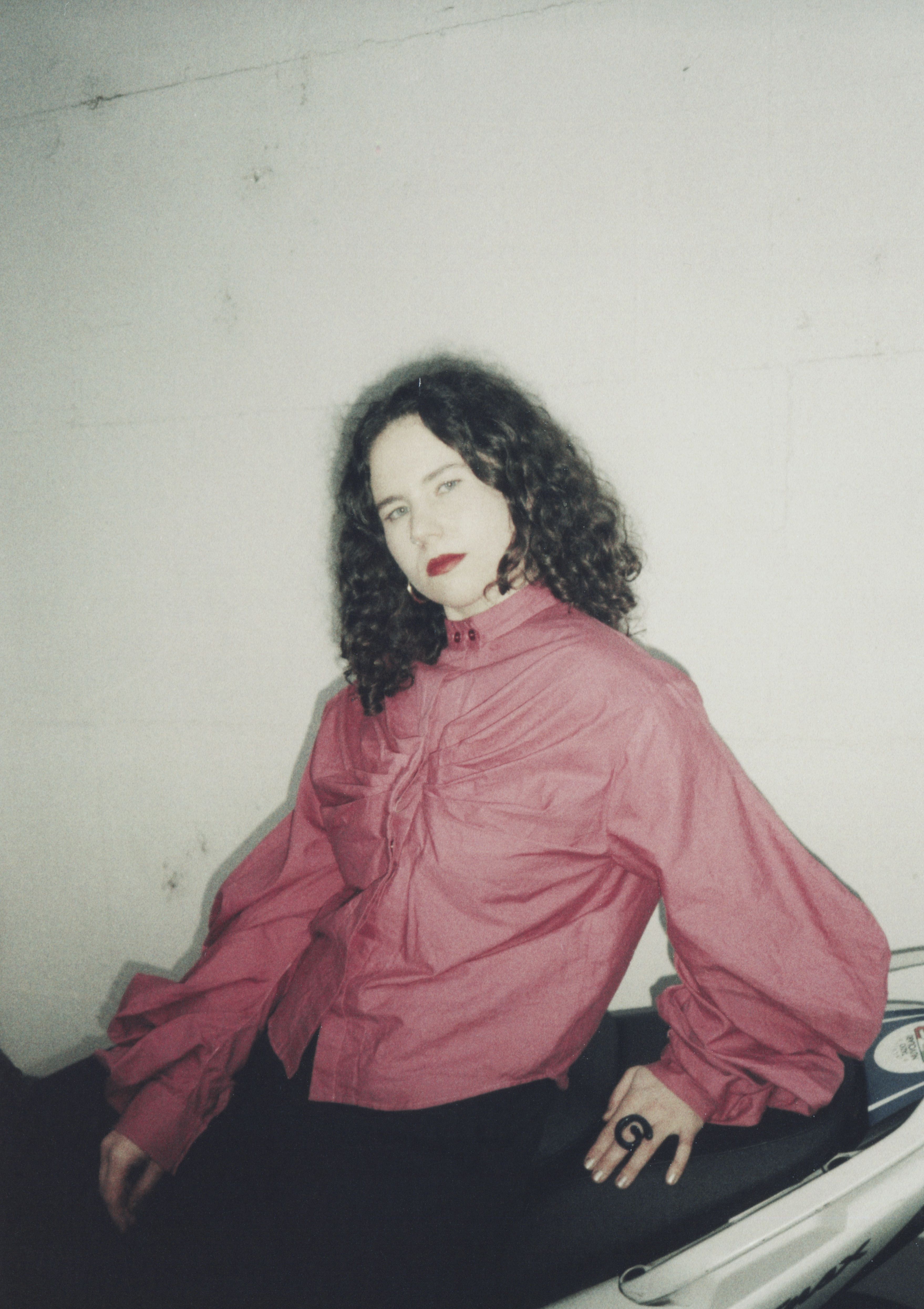 Eine Frau mit lockigen Haaren und einer roten Bluse sitzt auf einem Motorrad. Das ganze Bild ist nicht sehr scharf.