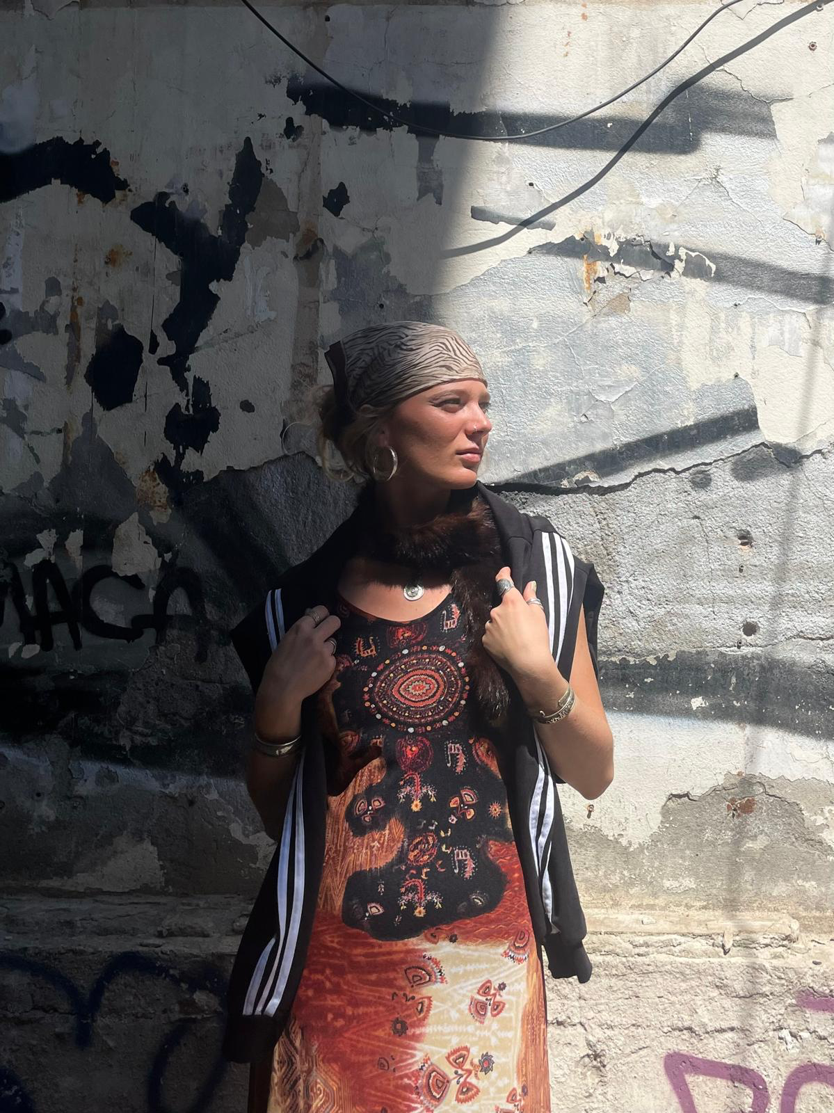 Frau mit Bandana im Halbschatten an einer Graffitiverschmierten Wand, sie schaut nach rechts und hält die Riemen ihres Rucksacks.