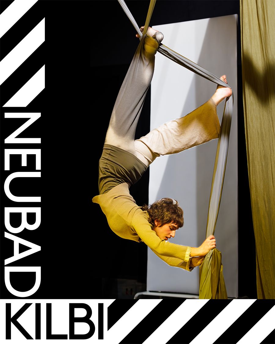 Eine Frau hängt kopfüber an einem Tuch für Vertikalseilakrobatik. Sie hat gelbe und beige Klamotten an.