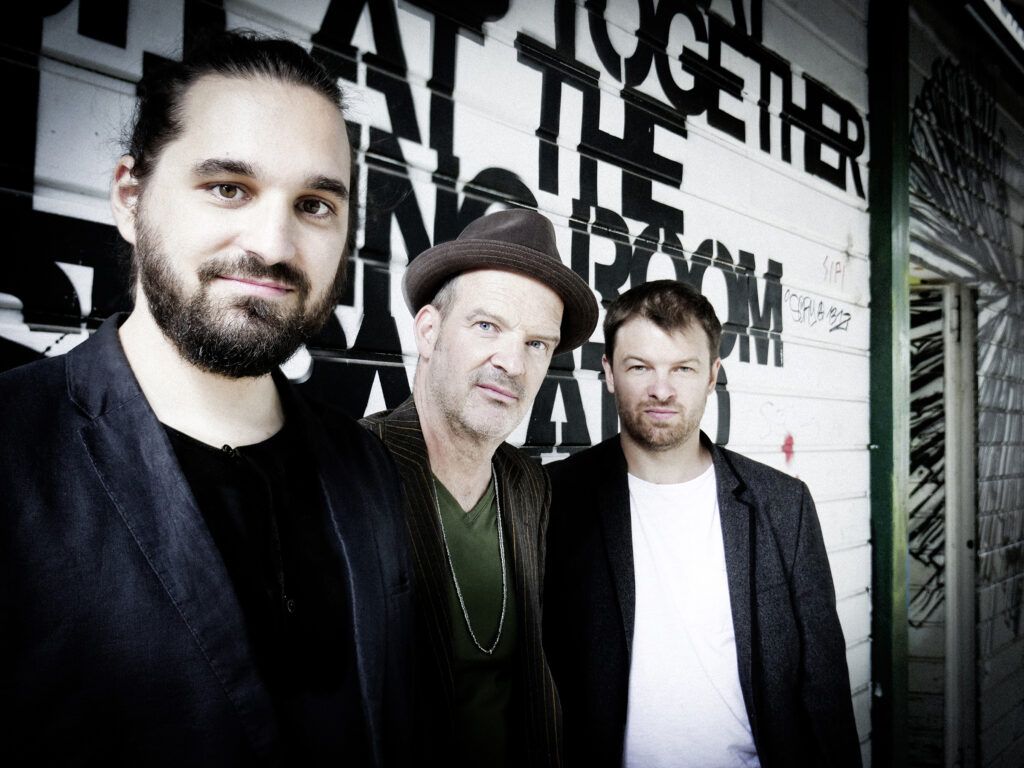 Drei Männer vor einer Wand mit Schrift. 