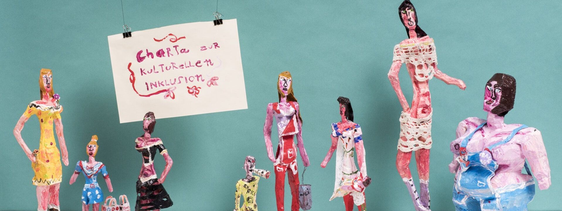 Farbenfrohe Lehmfiguren mit einem Plakat: Charta zur kulturellen Inklusion