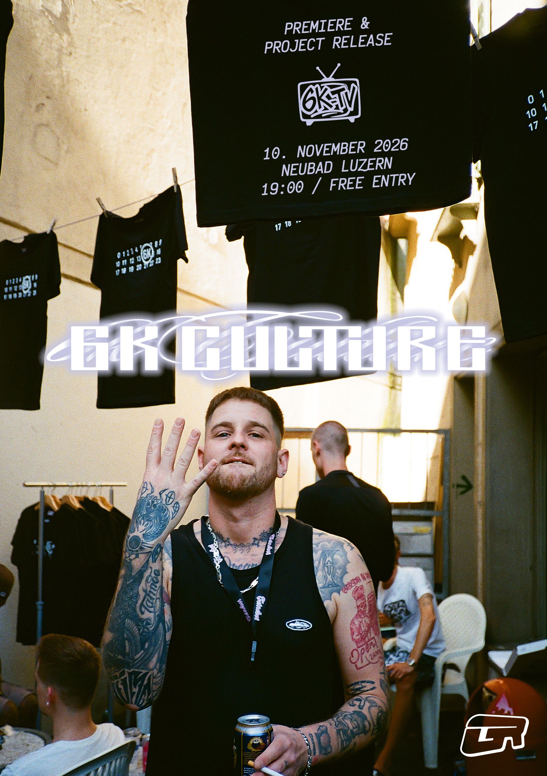 Ein Mann, der seine Hand hochhält und 4 Finger mit dem Handrücken zur Kamera hält. Über ihm hängen schwarze, weissbedruckte T-Shirts- Er trägt einen Tanktop und ist stark tätowiert.